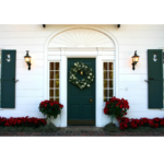 A white house with a green door with christmas decors and red flowers