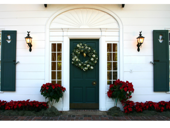 A white house with a green door with christmas decors and red flowers